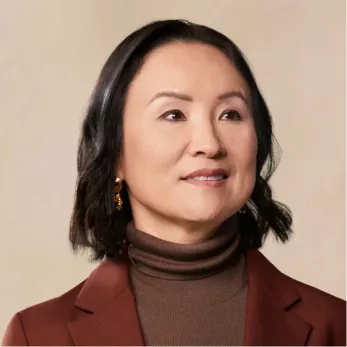 A headshot of an East Asian woman with dark, shoulder-length hair, wearing a brown turtleneck and blazer.
