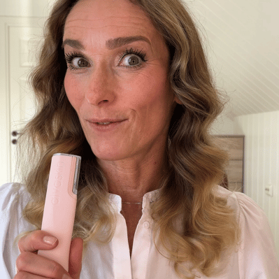 Person holding a pink device, smiling indoors.