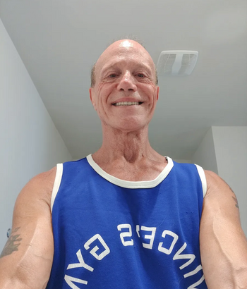 A person wearing a blue gym tank top, smiling at the camera indoors.