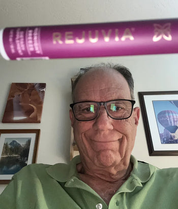 A person wearing glasses holds a Rejuvia product in front of the camera.