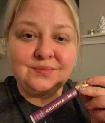A person holding a purple tube labeled 'REJUVA' in a home setting.