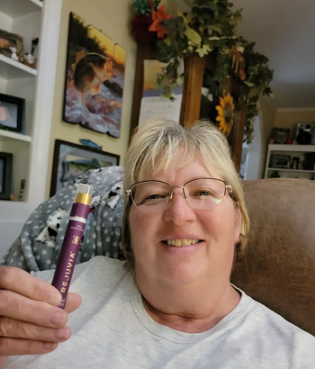 A person sitting on a couch holding a purple vape pen with a smile.