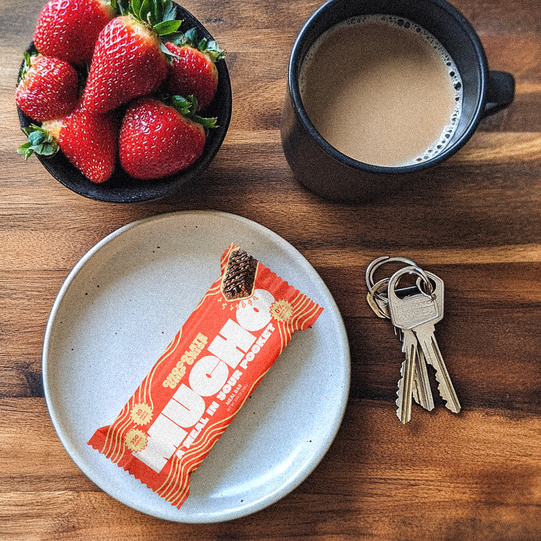 Plate with a snack bar, cup of coffee, strawberries, and keys on a table.
