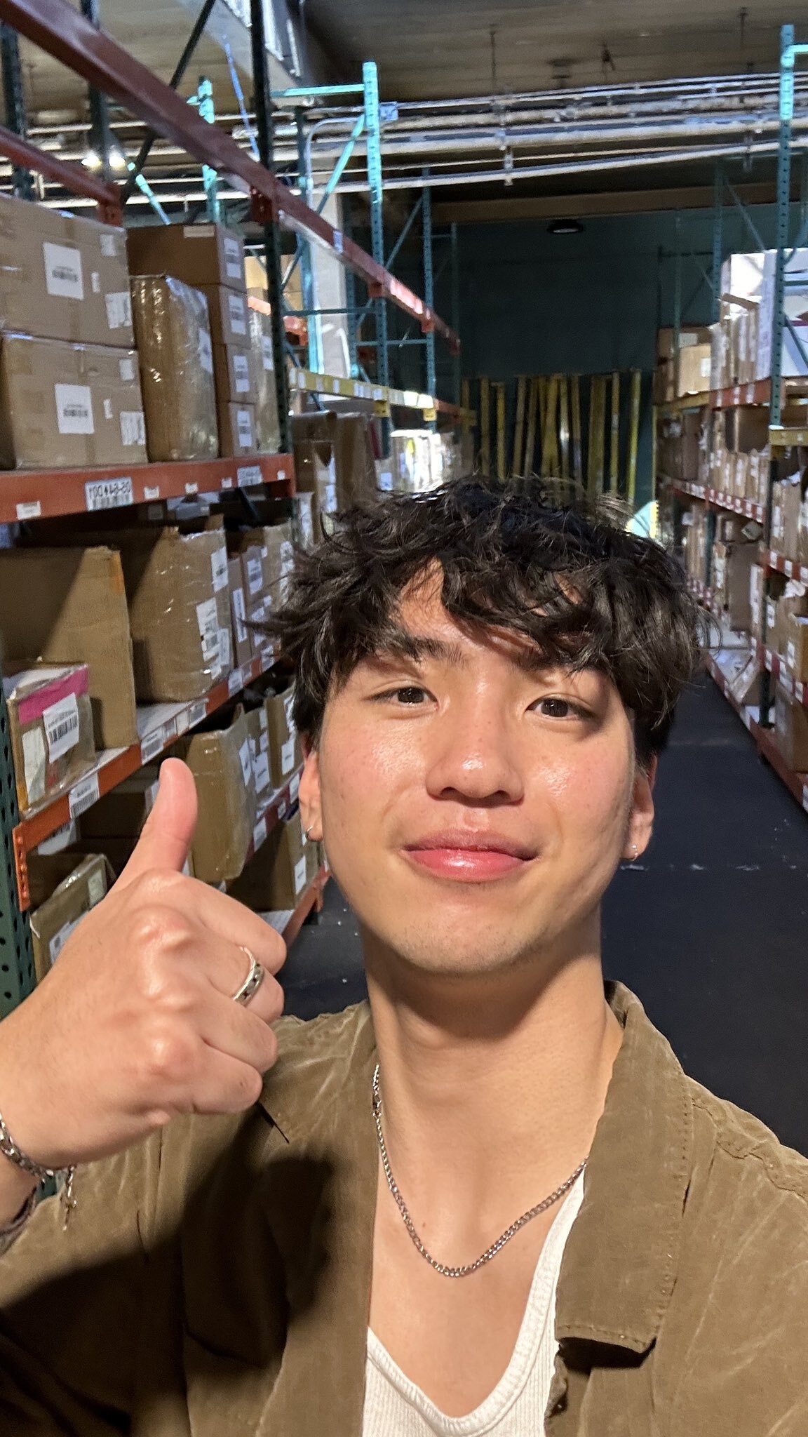 Person giving a thumbs up in a warehouse with shelves of boxes.