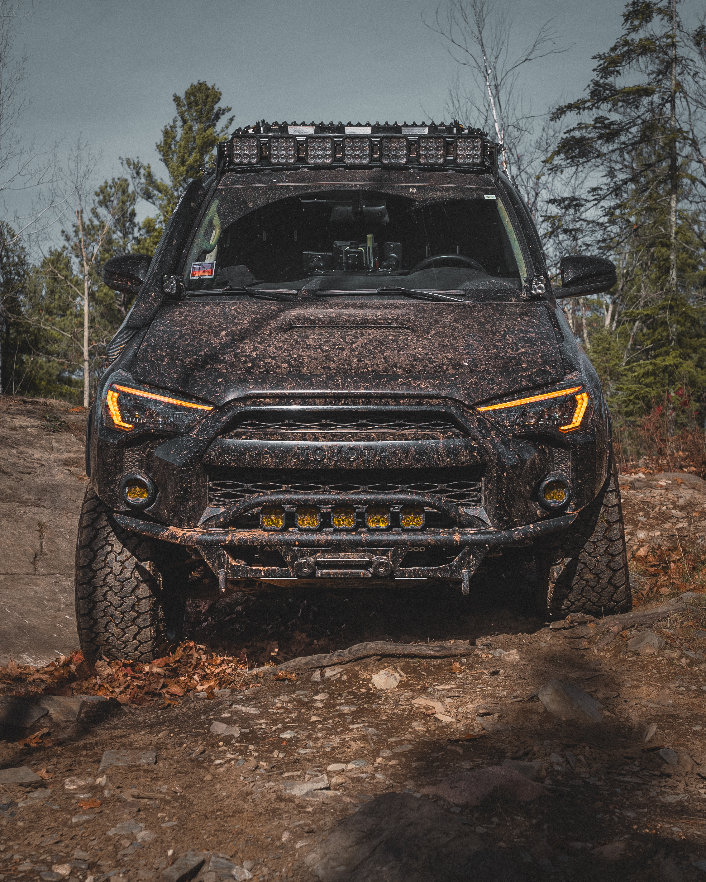 A muddy off-road vehicle on a rocky trail surrounded by trees.