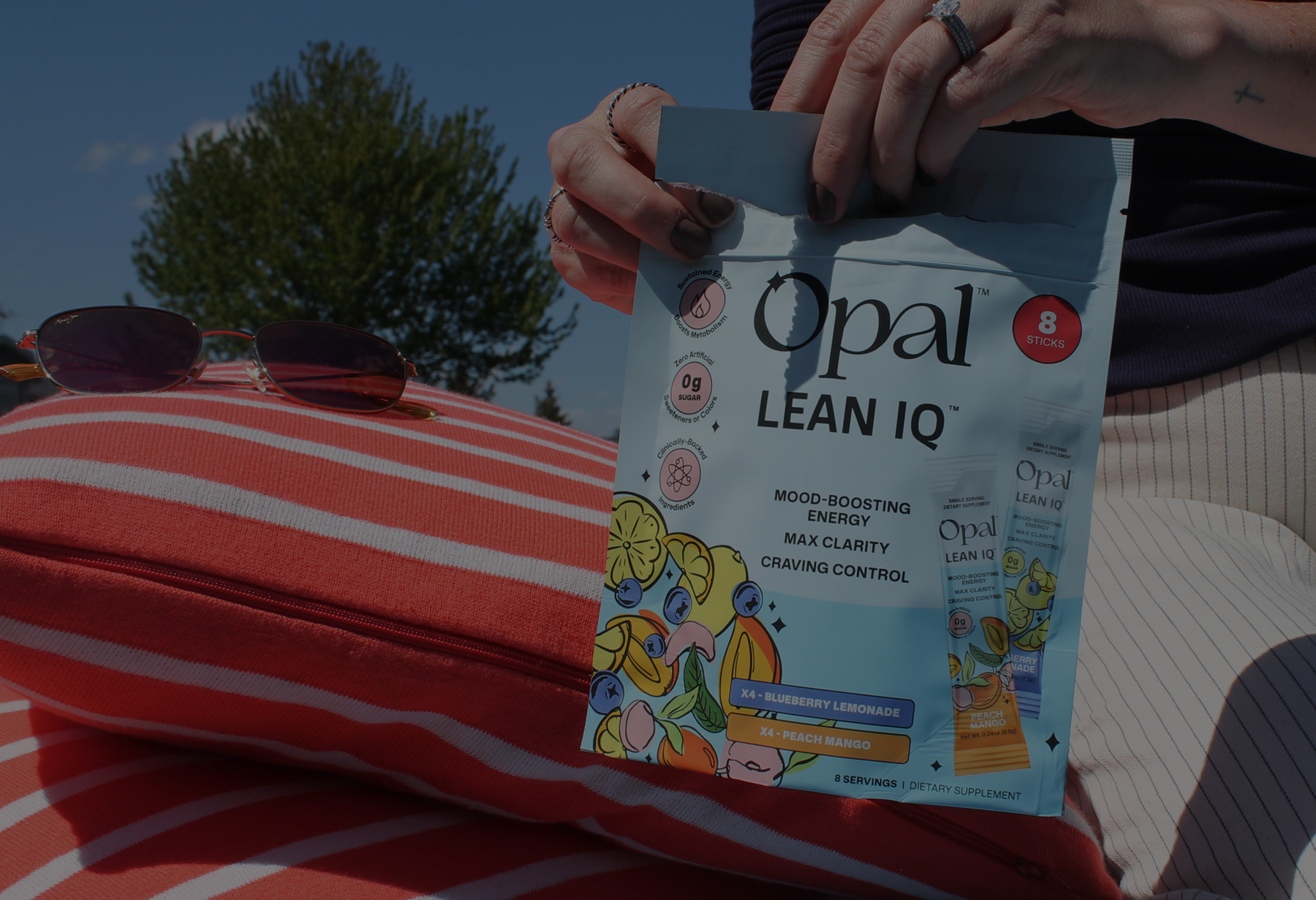 A person holds a pouch of Opal Lean IQ supplement outdoors next to a striped pillow and sunglasses.
