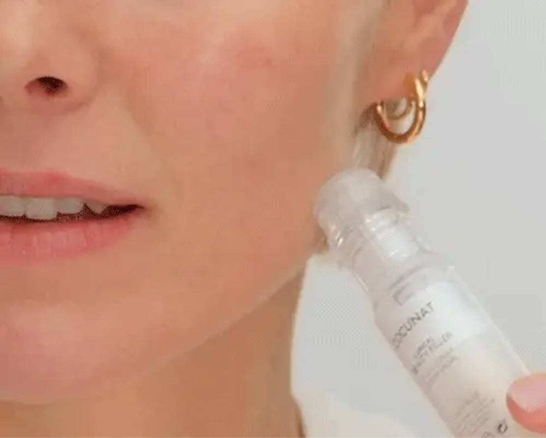 Person applying skincare product to their cheek with a roll-on bottle.