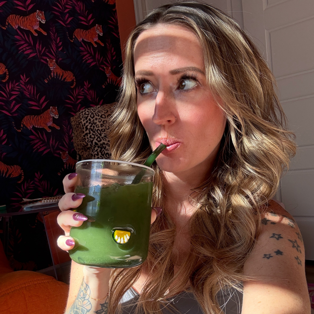 Person sipping a green drink in front of tiger-patterned wallpaper.