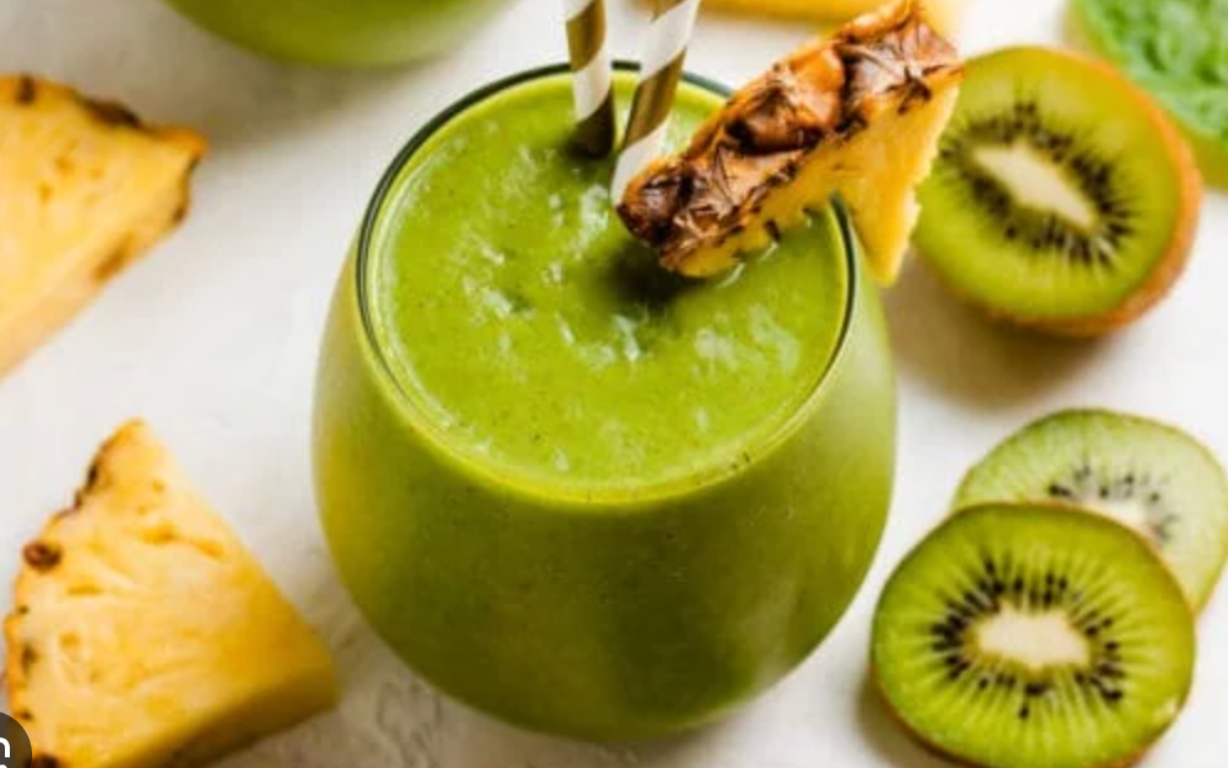 Green smoothie with pineapple slice, kiwi slices, and paper straws.