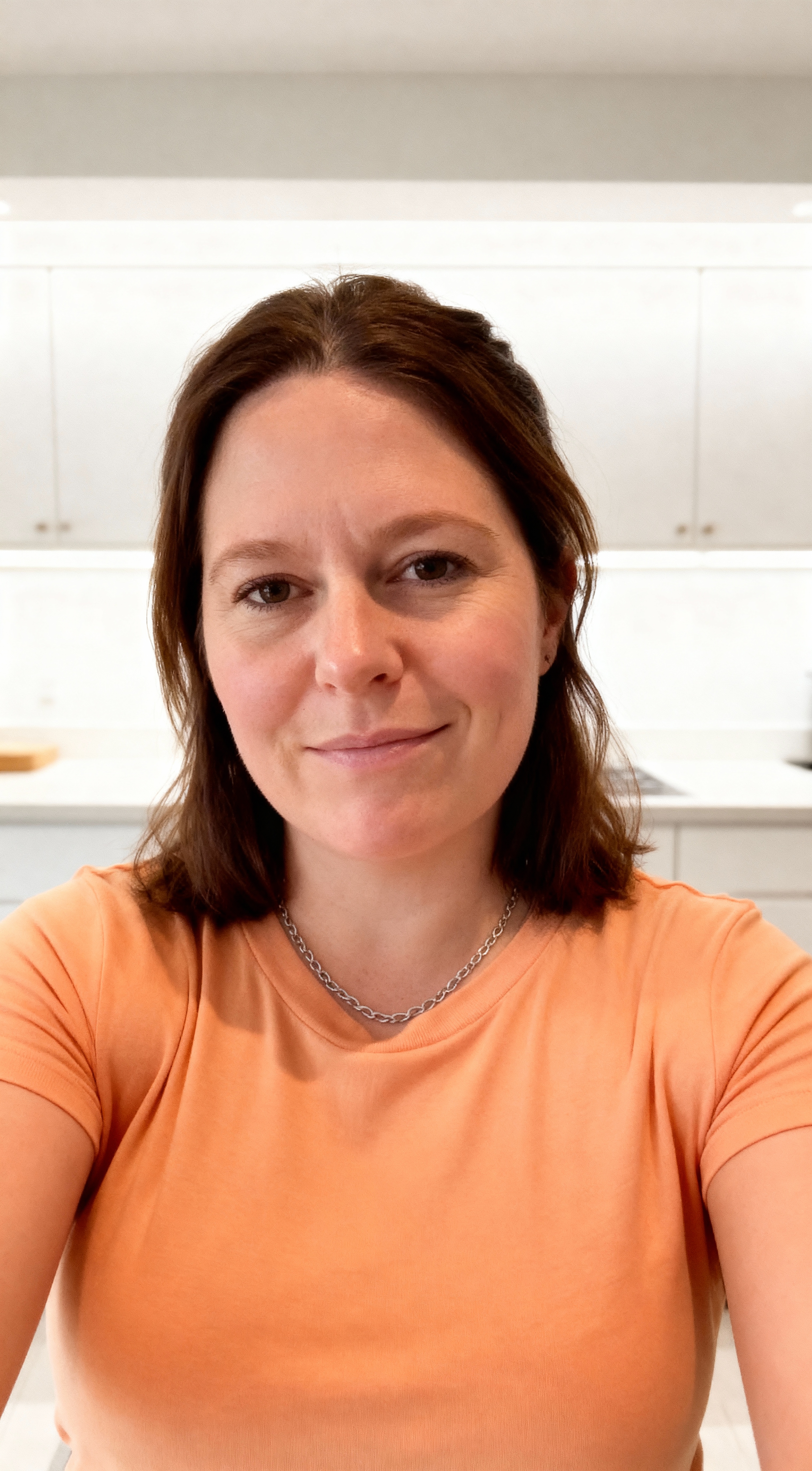 A person in an orange shirt standing in a bright kitchen.