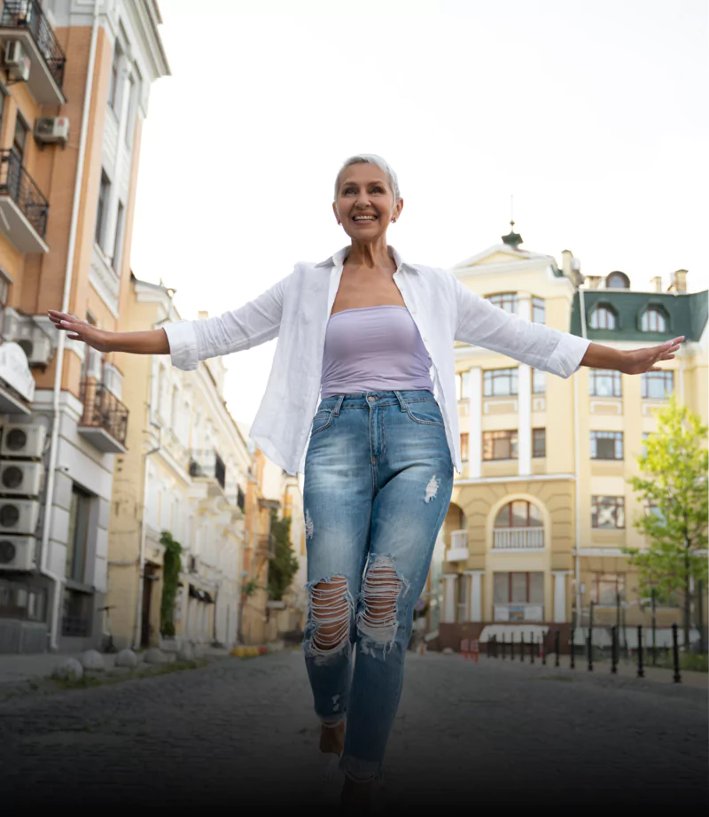 Smiling woman walking on a cobblestone street with arms outstretched.