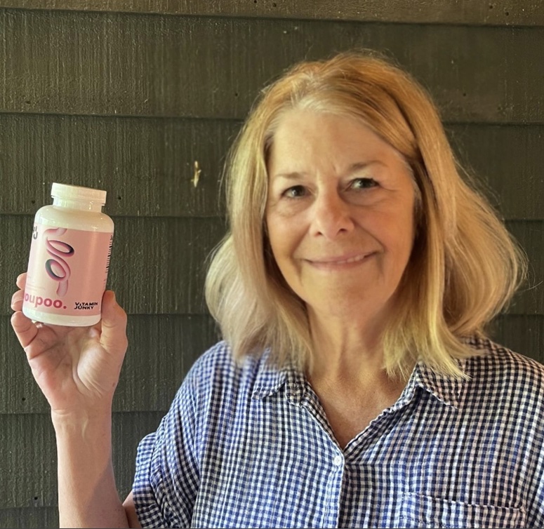 Person holding a bottle with a pink label, smiling at the camera.