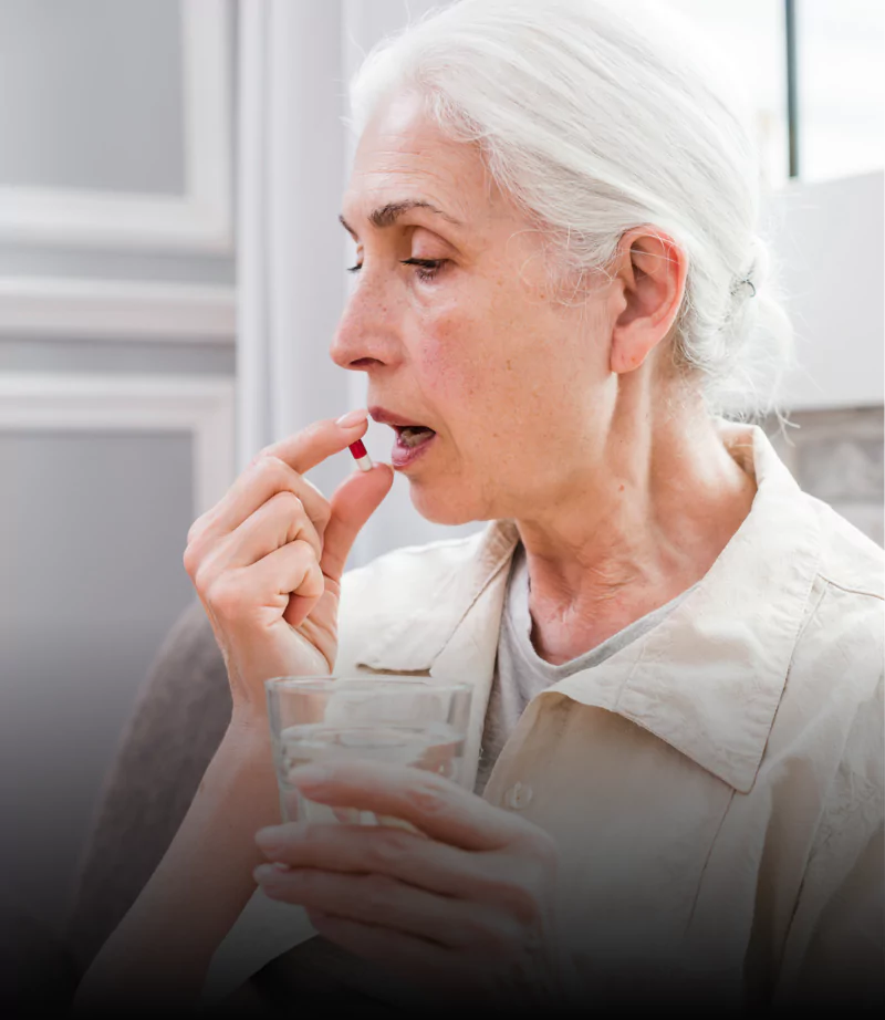 Elderly woman taking a pill with a glass of water.