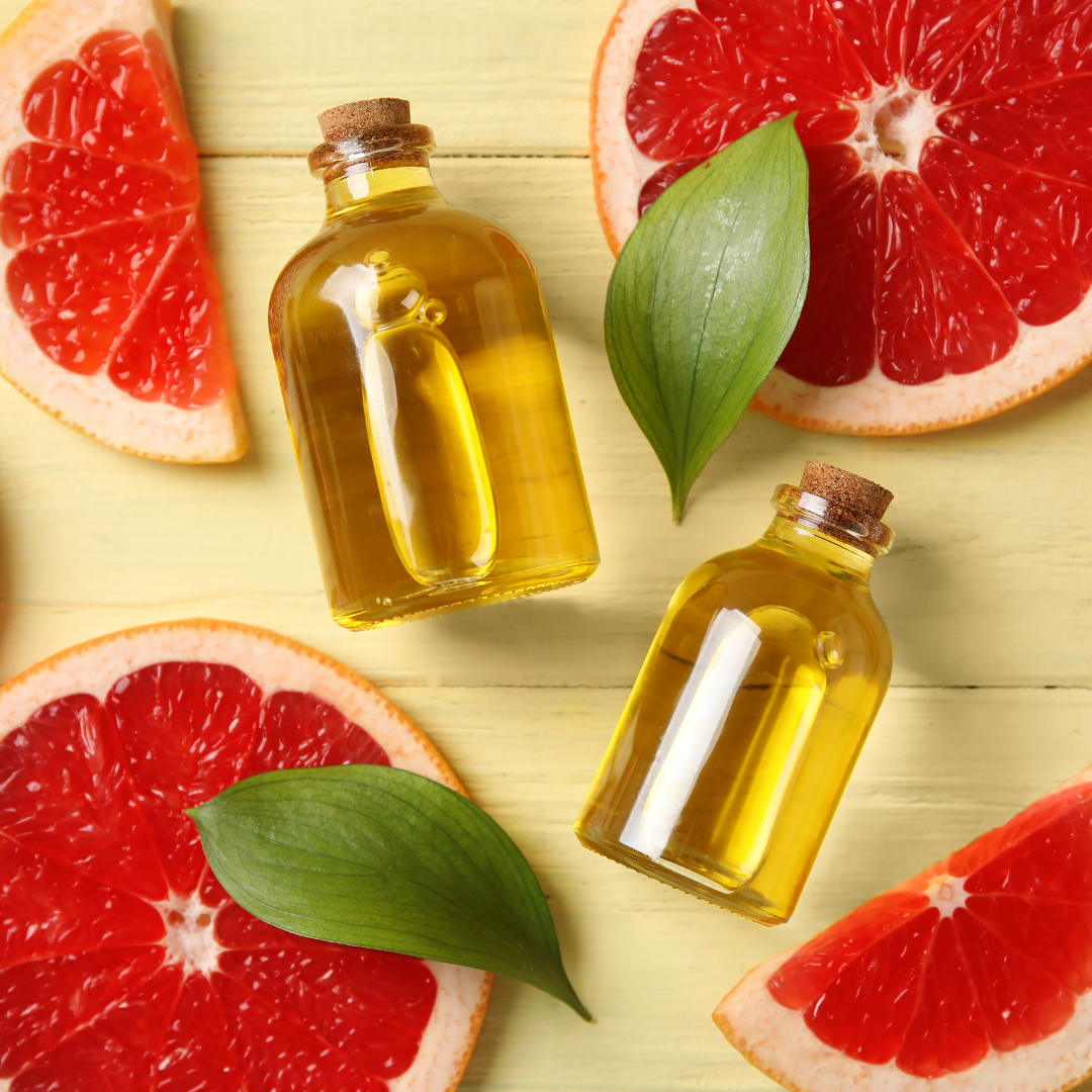 An overhead shot of two bottles of oil, slices of red grapefruit, and green leaves on a yellow surface.