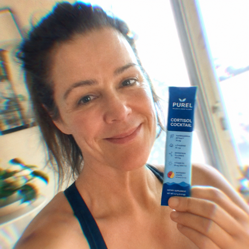 A smiling woman holds up a blue packet of Purel Cortisol Cocktail dietary supplement.