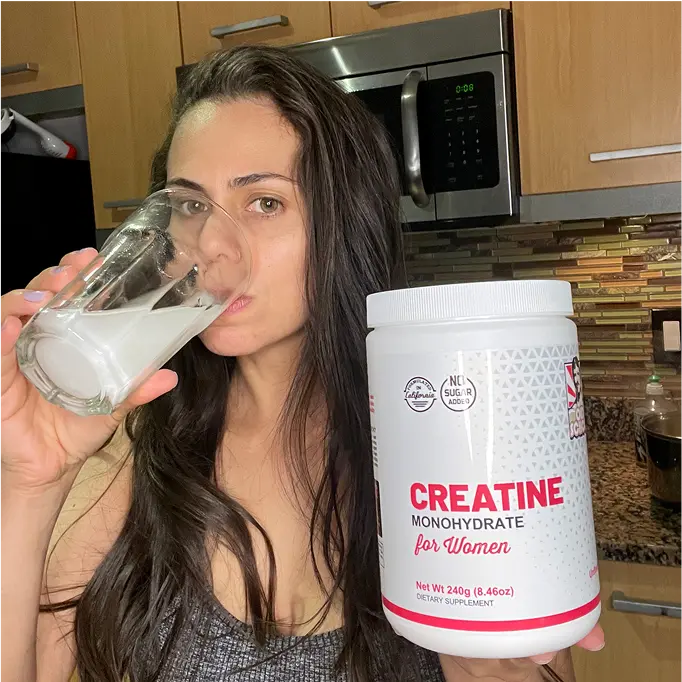 Person drinking from glass beside creatine container in kitchen.