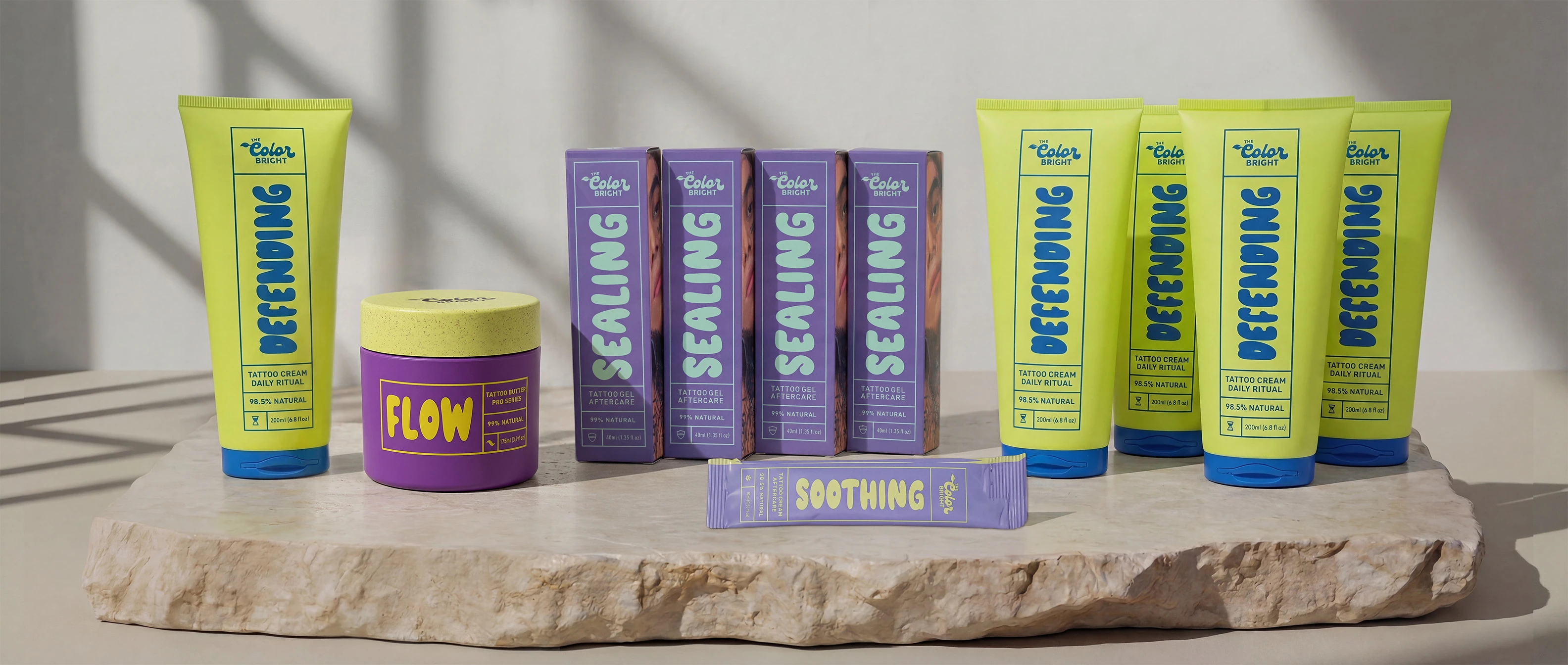 A heavily tattooed man holds a collection of colorful tattoo aftercare products against his chest.