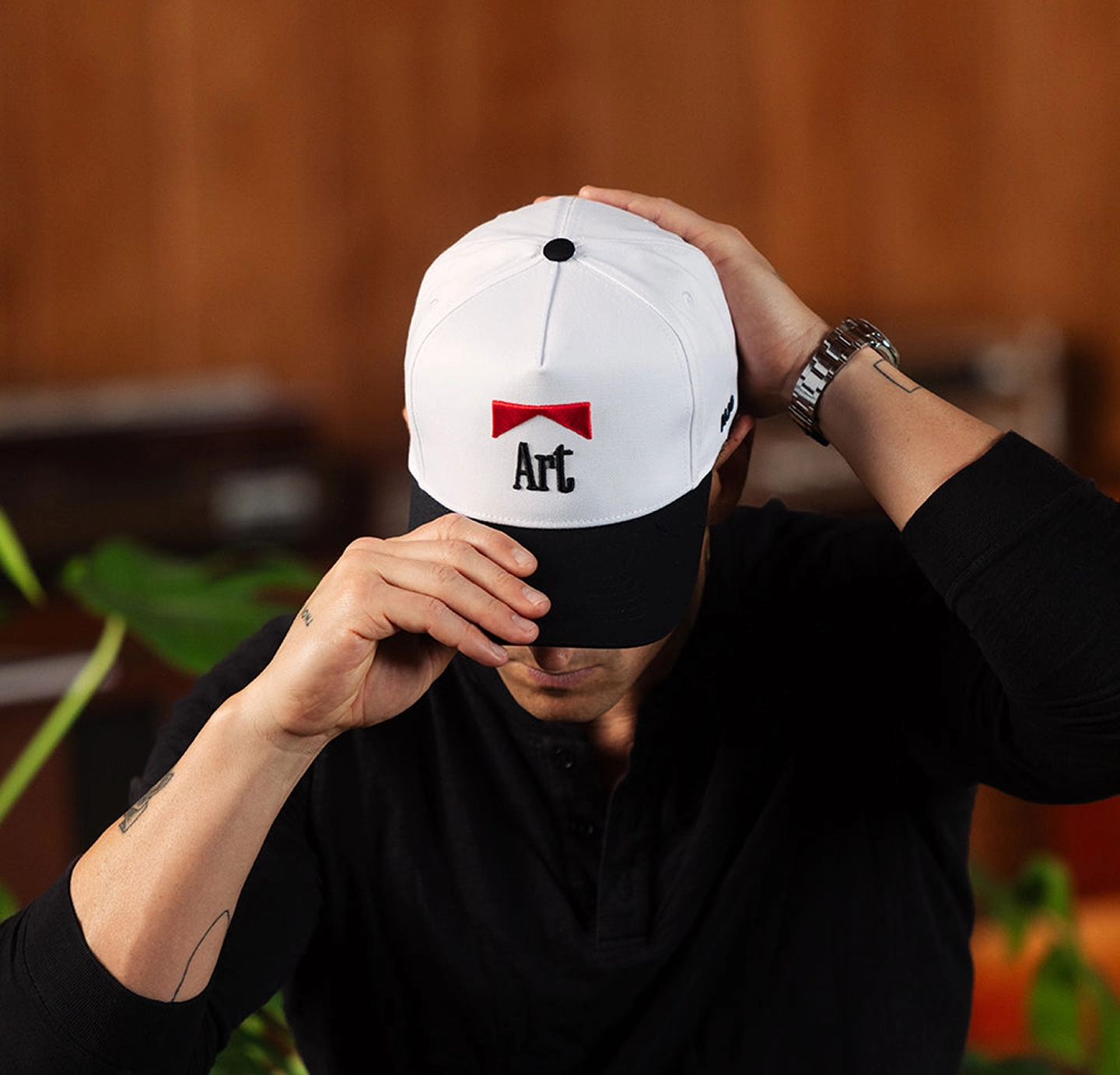 Person wearing a white cap with 'Art' text, adjusting it with both hands.