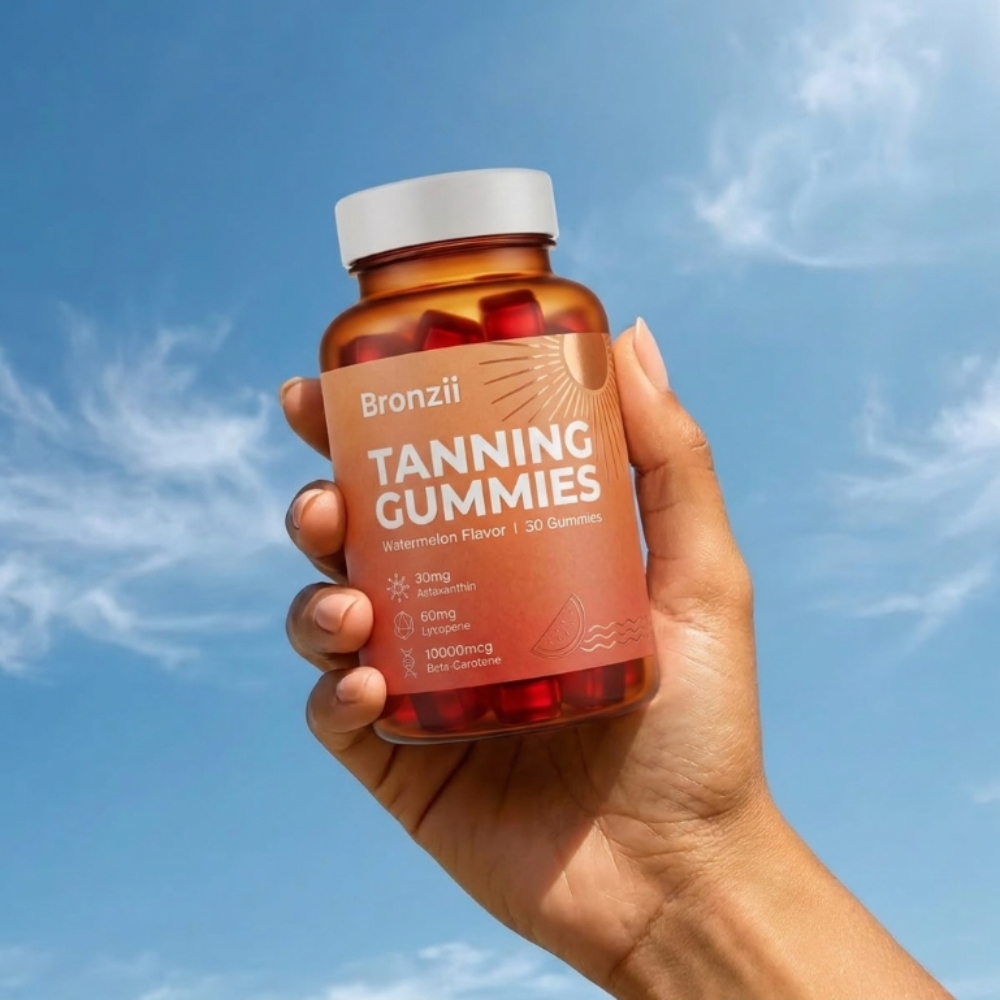 A hand holds a bottle of Bronzii Tanning Gummies against a bright blue sky with wispy clouds.