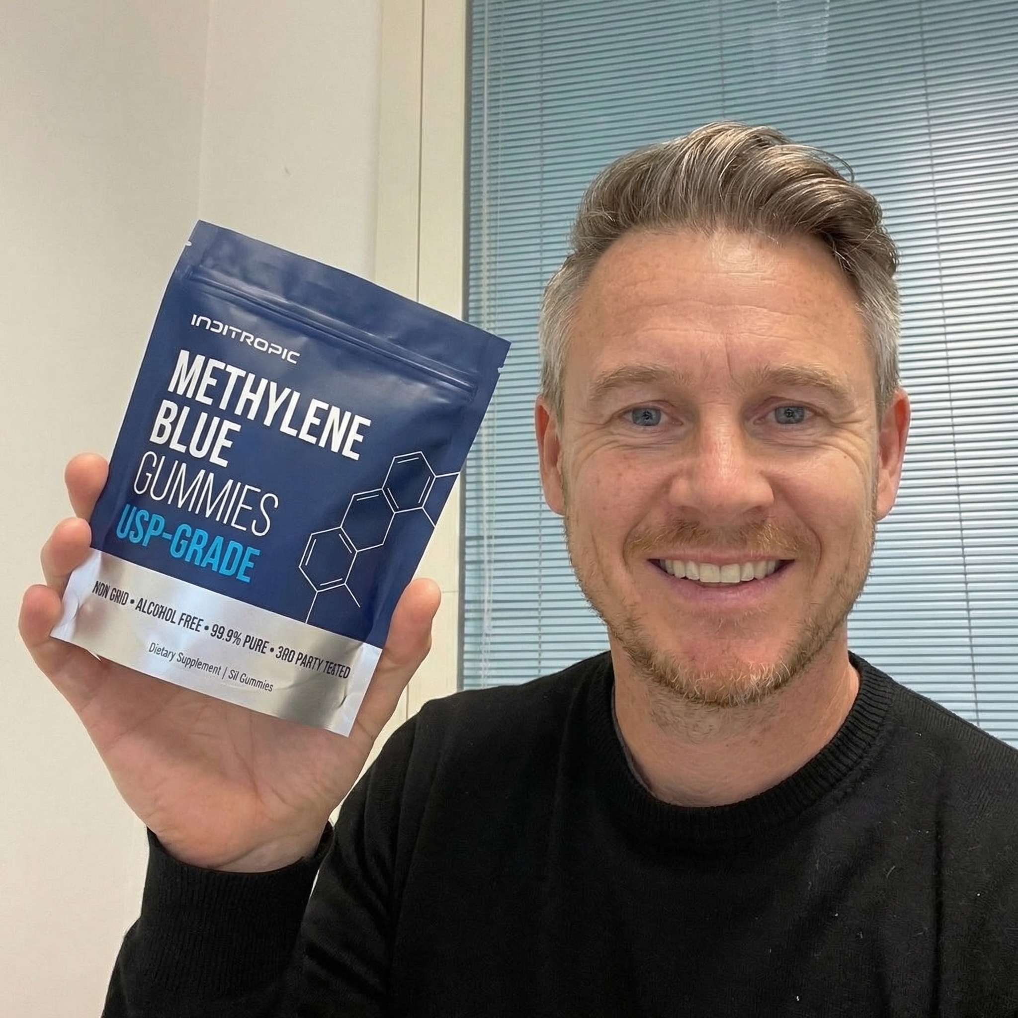 A smiling man with graying hair holds up a blue pouch of Inditropic Methylene Blue Gummies.