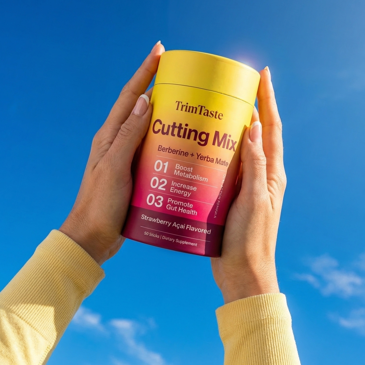A person holds a container of TrimTaste Cutting Mix dietary supplement against a bright blue sky.