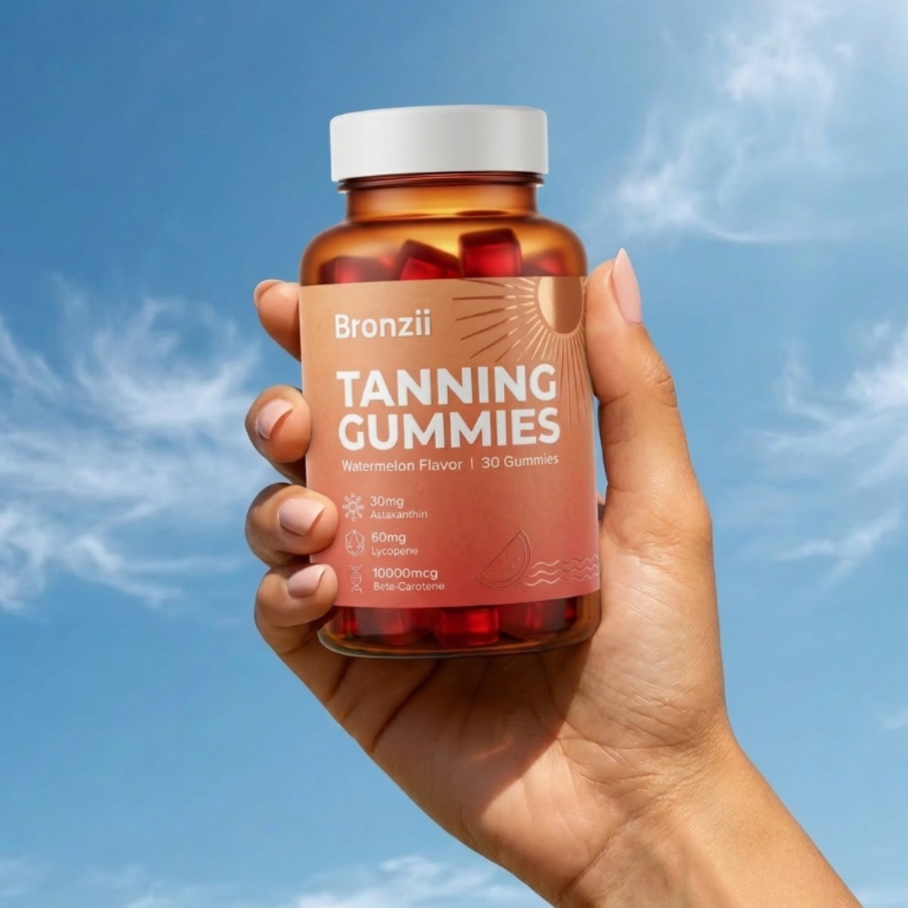 A hand holding a bottle of Bronzii Tanning Gummies against a blue sky with light clouds.