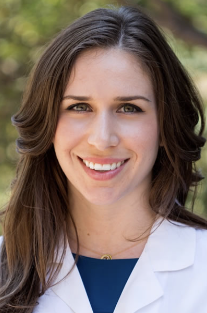 Smiling person in a white coat with long brown hair.