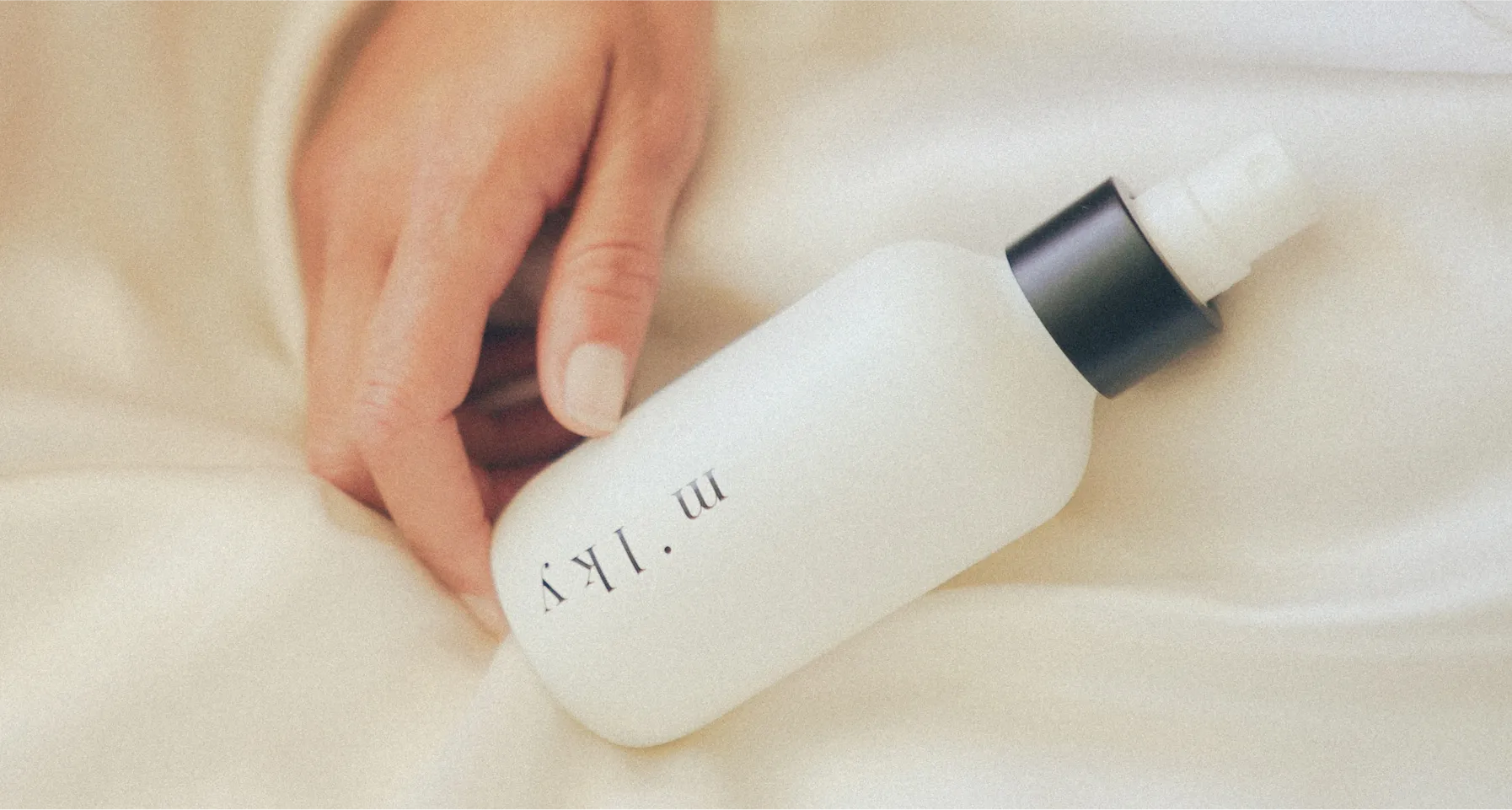 Hand holding a white spray bottle with black cap.