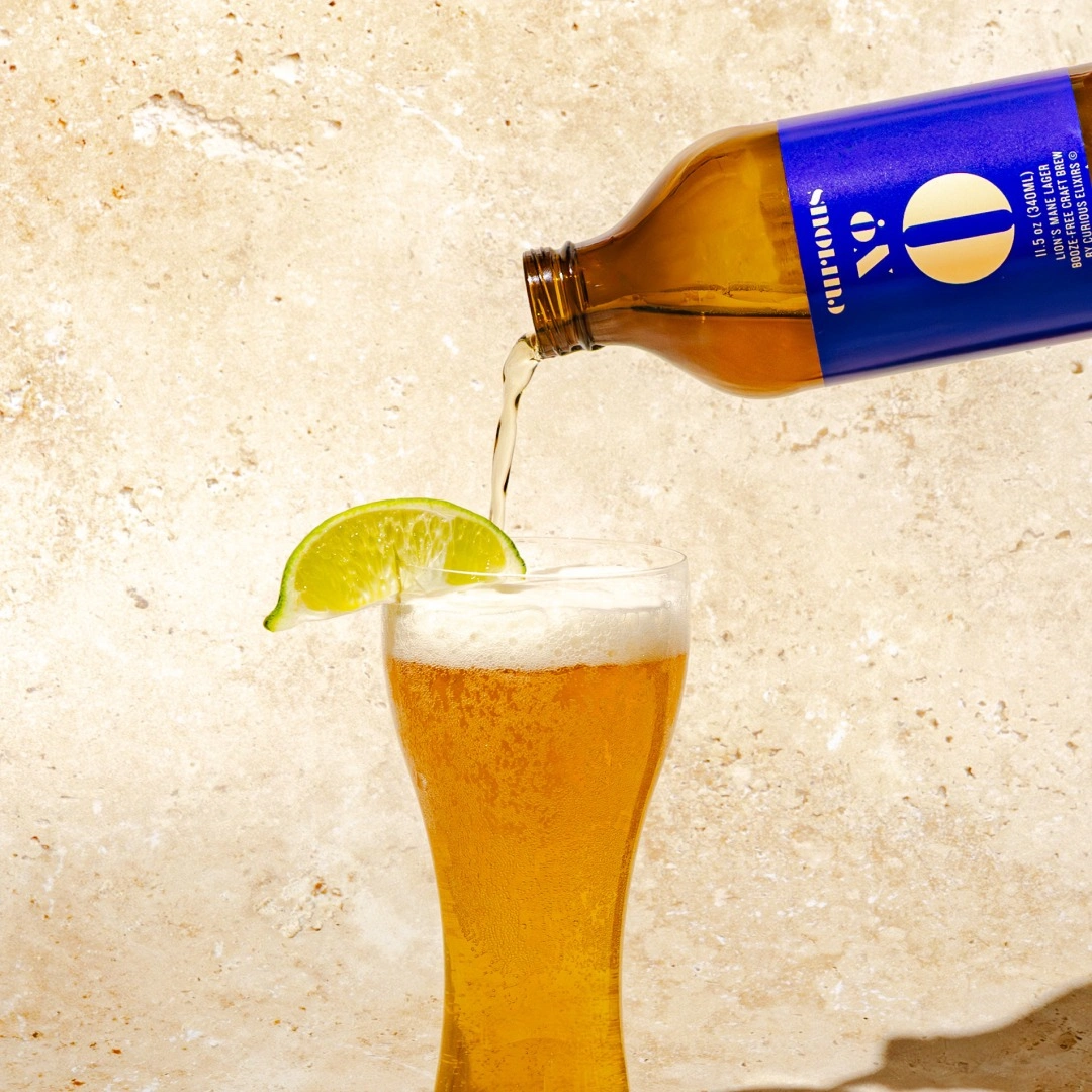 A beverage being poured from a bottle into a pilsner glass garnished with a lime wedge.