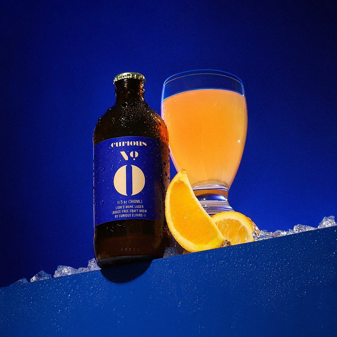 A bottle of Curious No. 0 craft brew next to a glass of the drink with orange slices on ice.