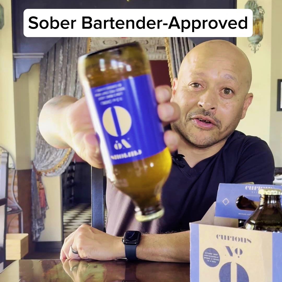 A man holds up a bottle of a beverage with a blue label, with text overlay 'Sober Bartender-Approved.'