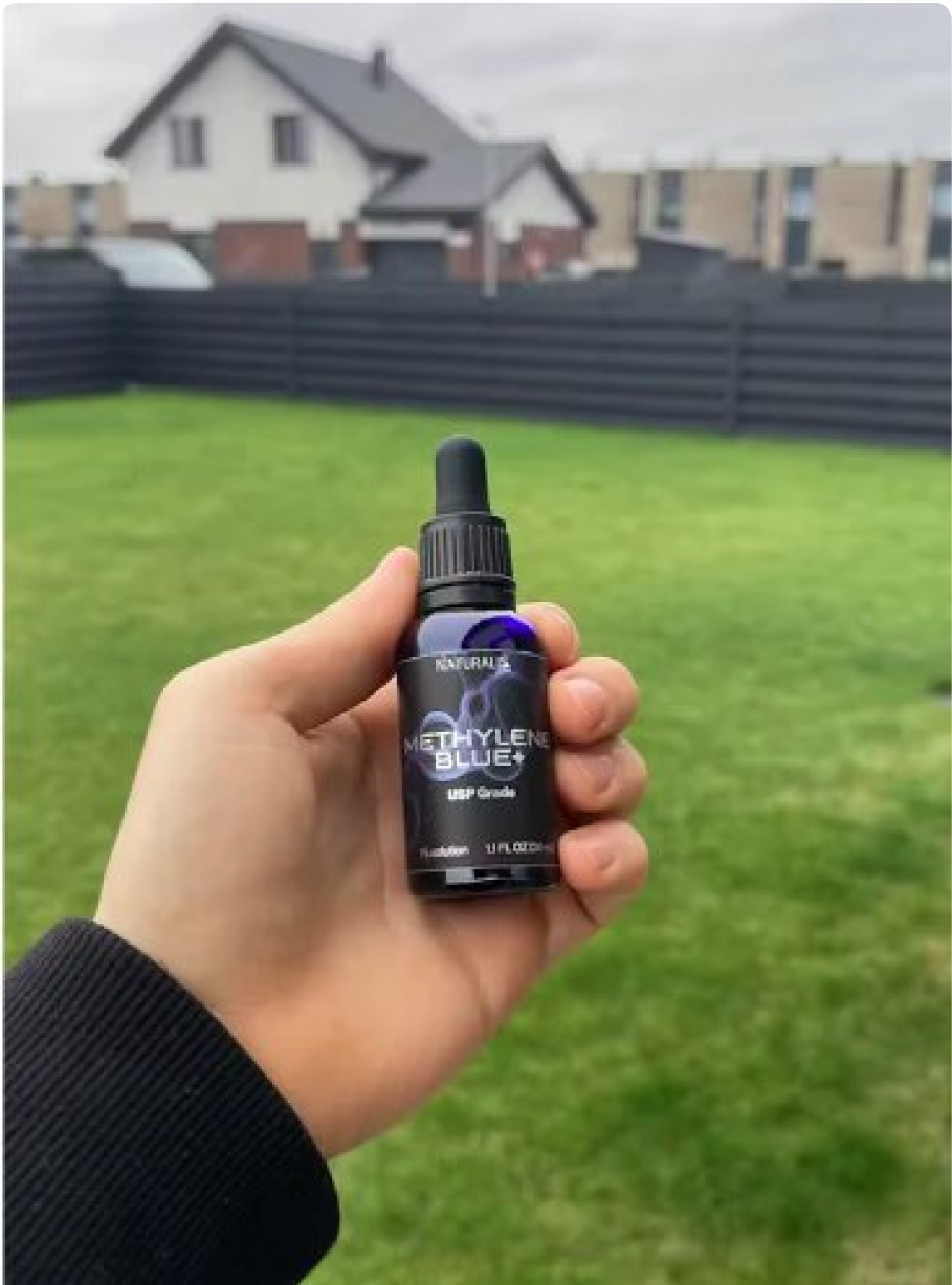 Hand holding a bottle labeled 'Methylene Blue+' in a grassy backyard.