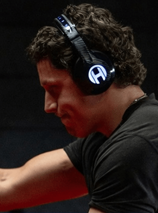 A man with curly hair is shown in profile, wearing large headphones with a glowing logo.