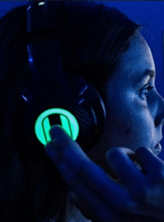 A close-up of a person touching a glowing logo on the side of their over-ear headphones.