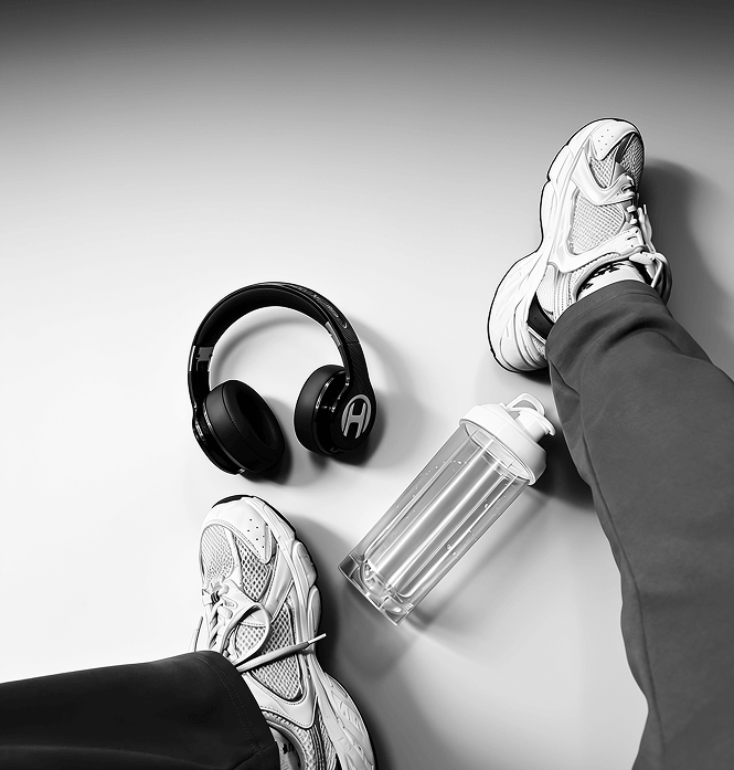 A black and white overhead shot of headphones, a water bottle, and a person's feet in sneakers.