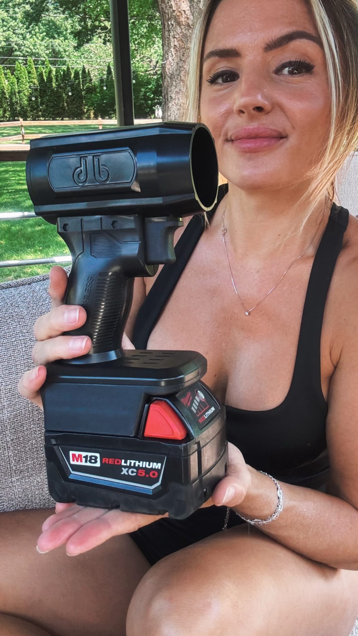 A woman in a black top holds a large, black, cordless power tool with a battery pack.