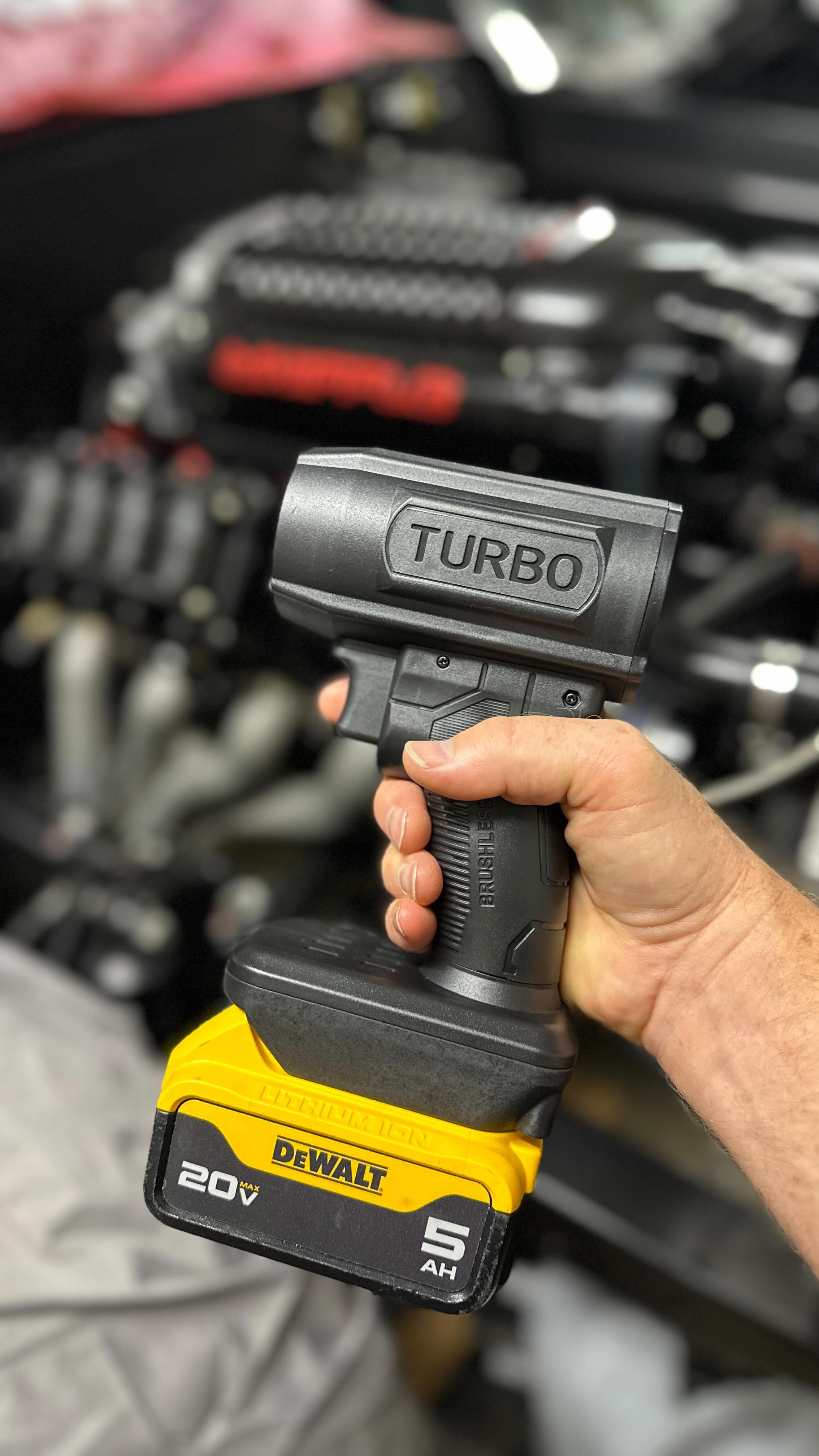A hand holding a black cordless tool labeled 'TURBO' with a yellow DeWalt battery attached.