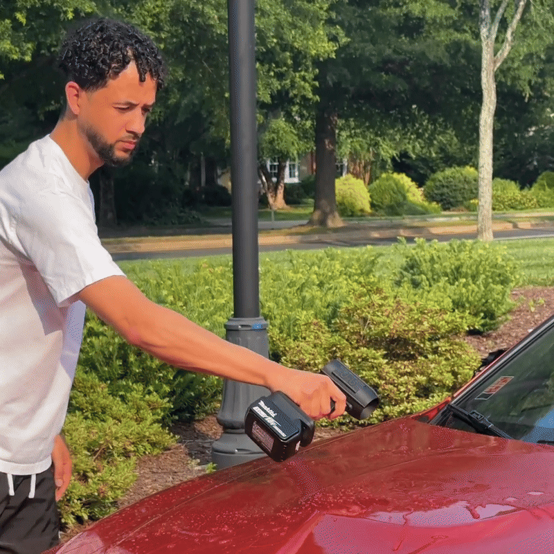 Person using a cordless polisher on a red car's hood outdoors.