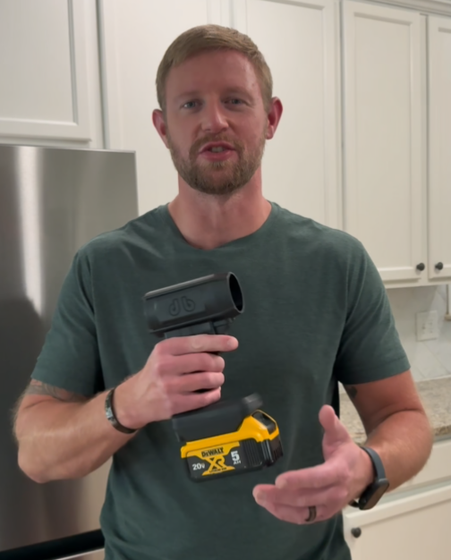 Person in kitchen holding a power tool with a yellow battery.