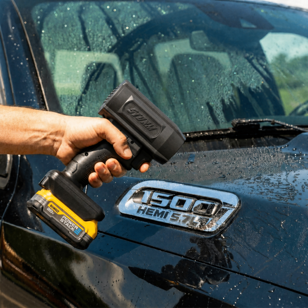 A person holds a cordless blower over the wet hood of a black Ram 1500 truck.