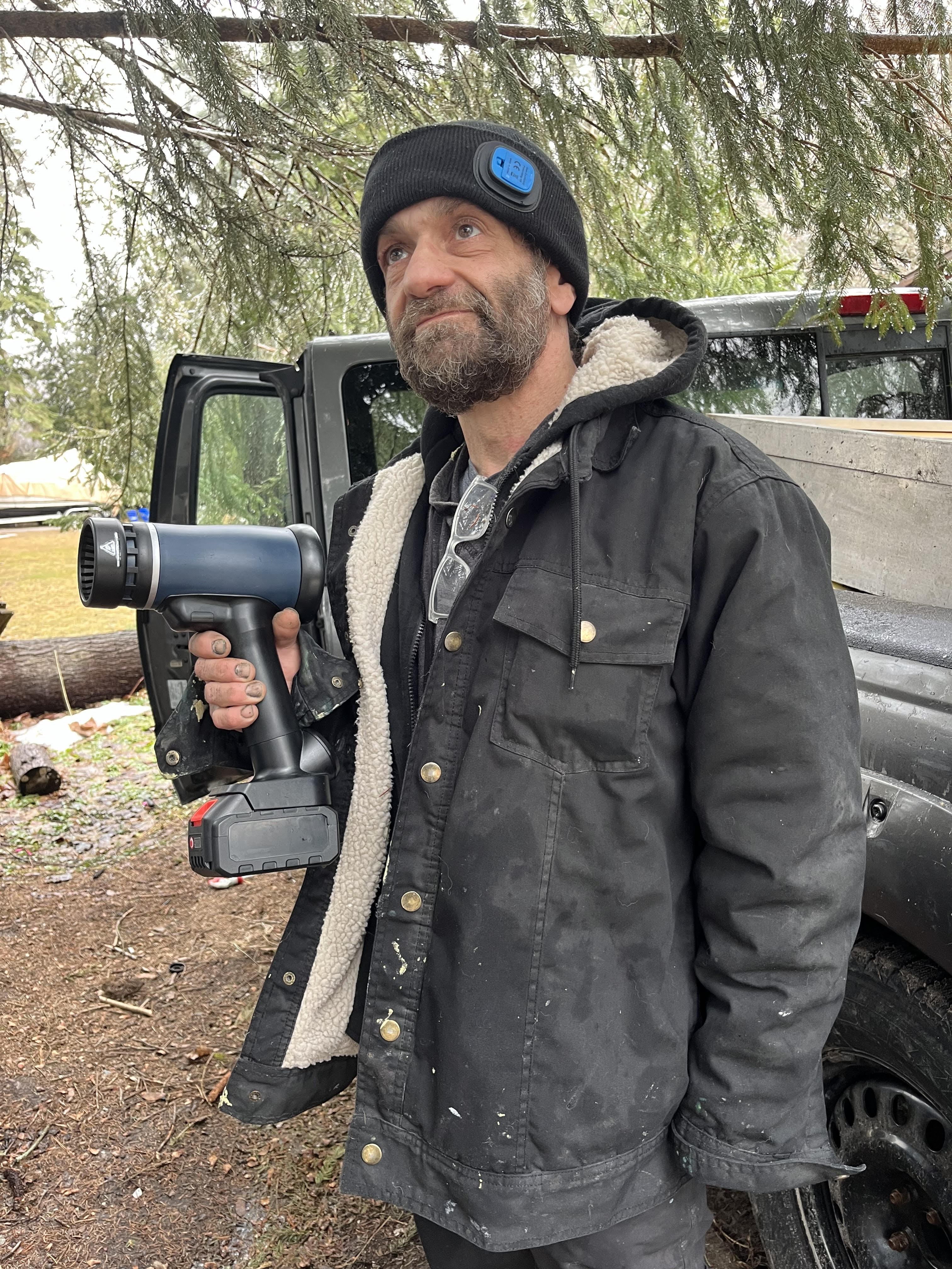 Person in a black jacket holding a power tool outdoors.