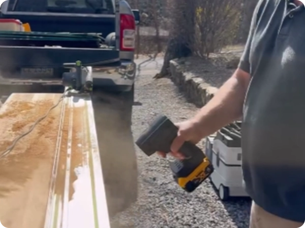 A person uses a cordless blower to clear sawdust from a board being cut with a track saw.