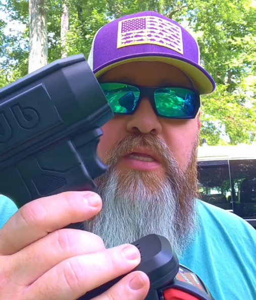 Person holding a black object with trees in the background.