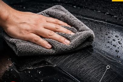 A hand wipes a wet, glossy black surface with a grey microfiber cloth, leaving streaks behind.