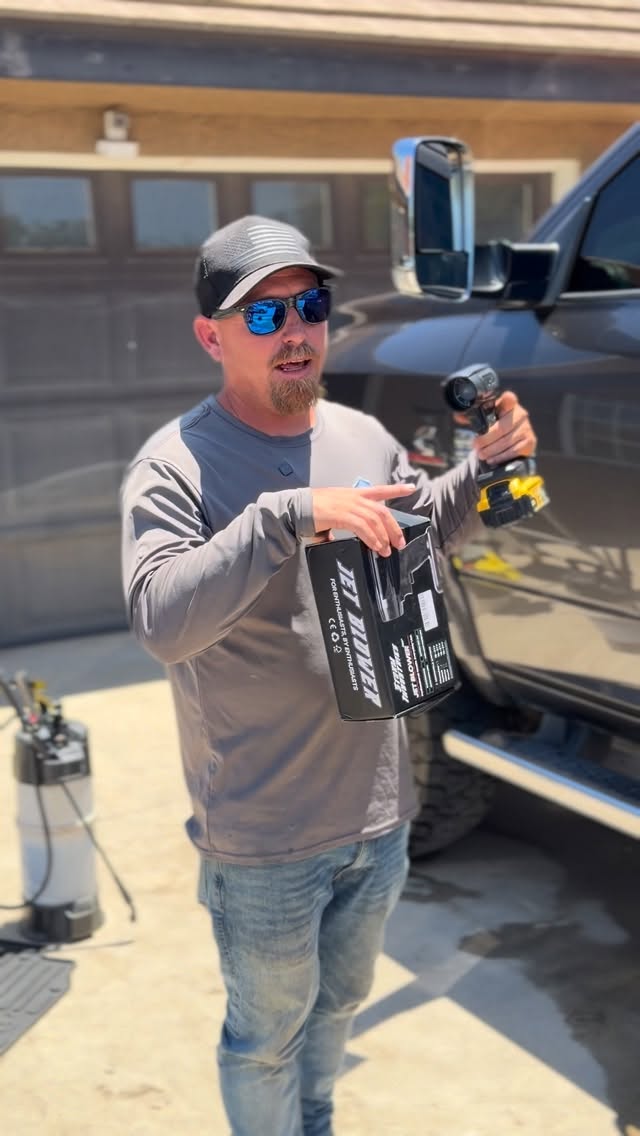 A man in sunglasses holds a small cordless blower and its box in front of a truck.
