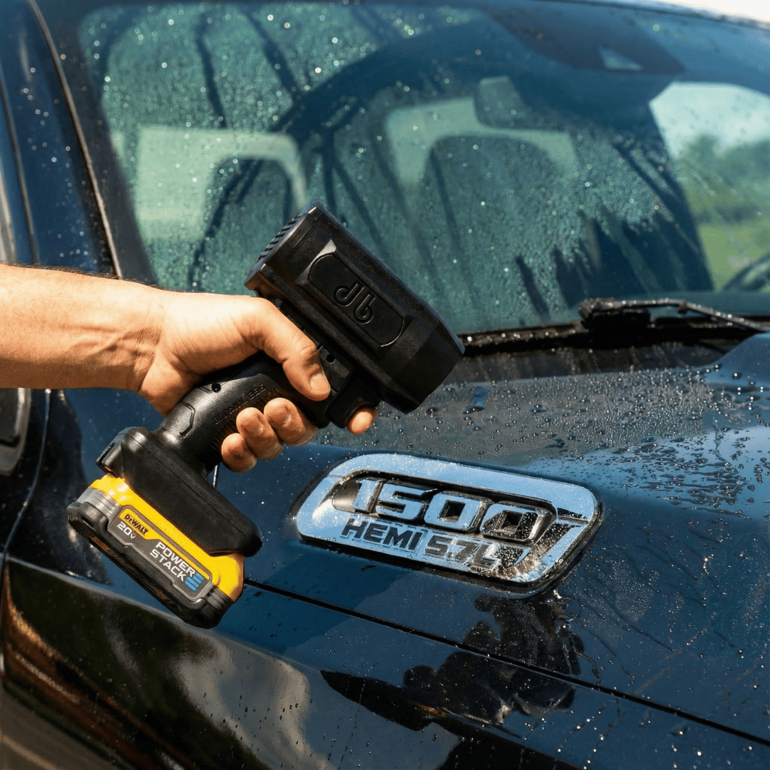 A hand holding a battery-powered blower to dry a wet black truck after a wash.