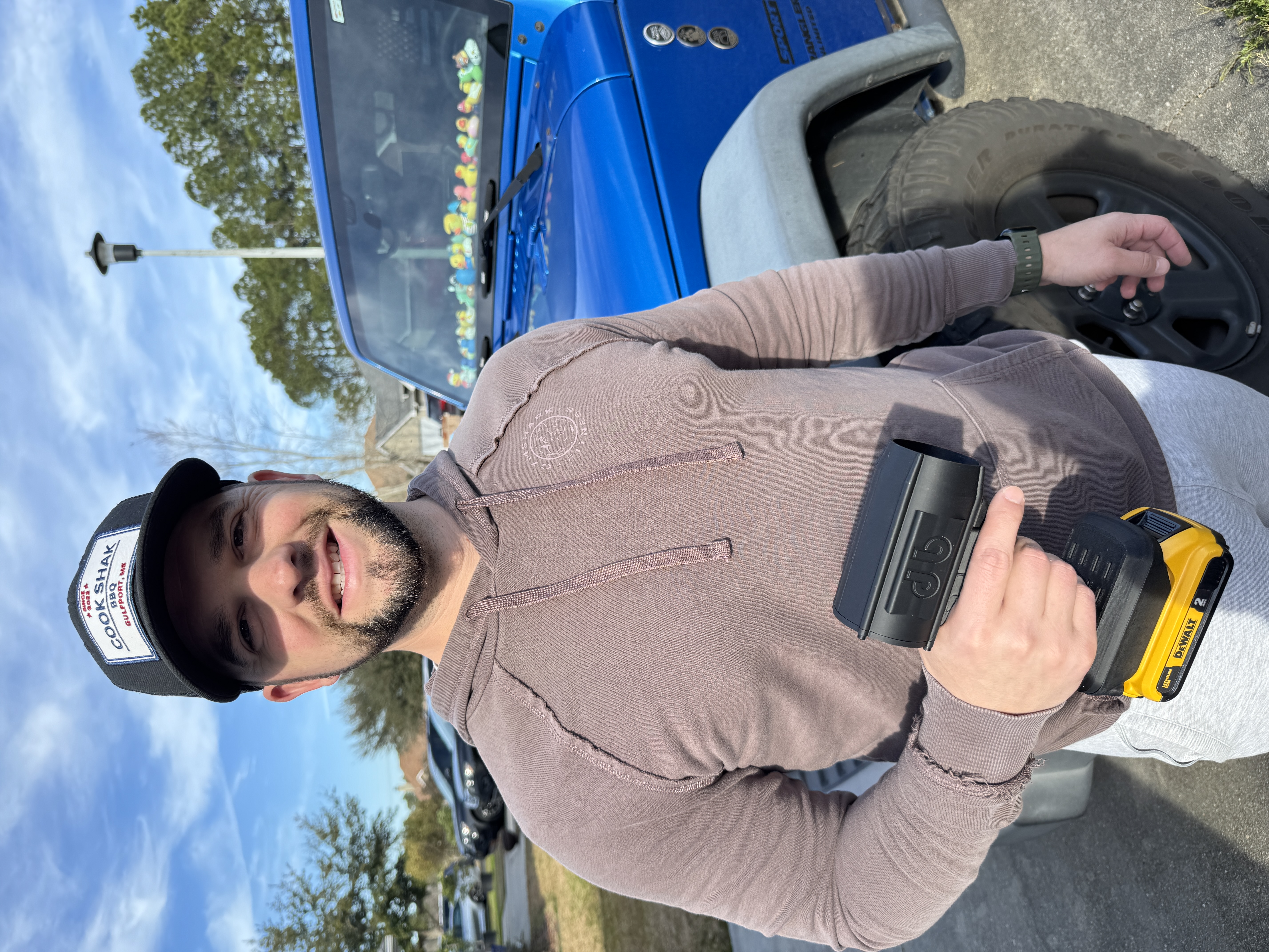 Man holding a tool, standing next to a blue vehicle with toy figures on the dashboard.