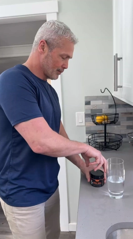Man in kitchen opening a container next to a glass of water.