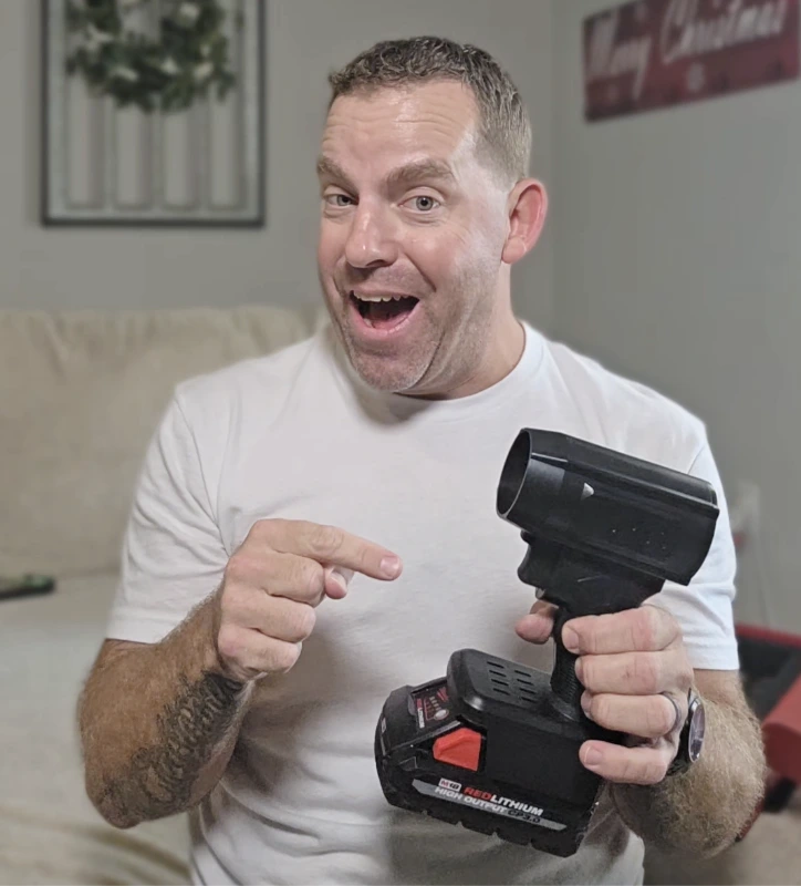 Person smiling and pointing at a tool with a battery.