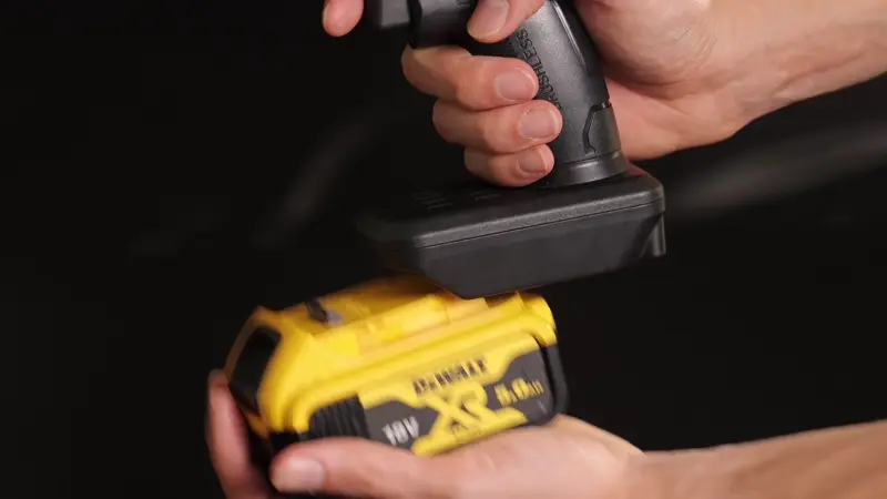 Hands attaching a yellow power drill battery.